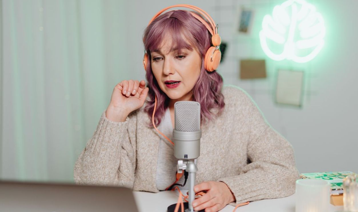 Woman podcaster in a cozy room speaking into a microphone, wearing headphones.