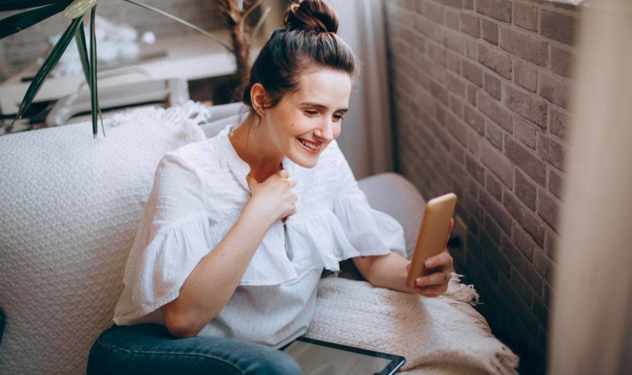 Cheerful woman having a video call on her smartphone while relaxing on a cozy sofa indoors.