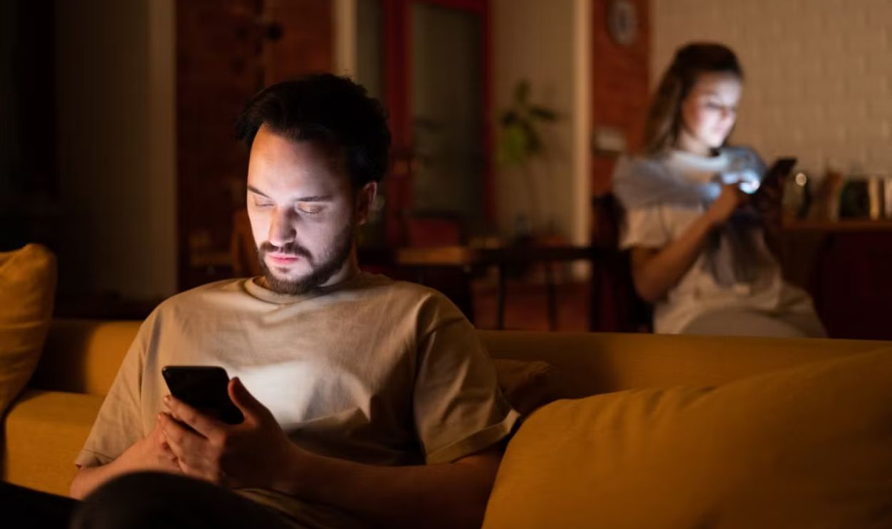A couple enjoying a cozy evening in a warm home, both using smartphones.