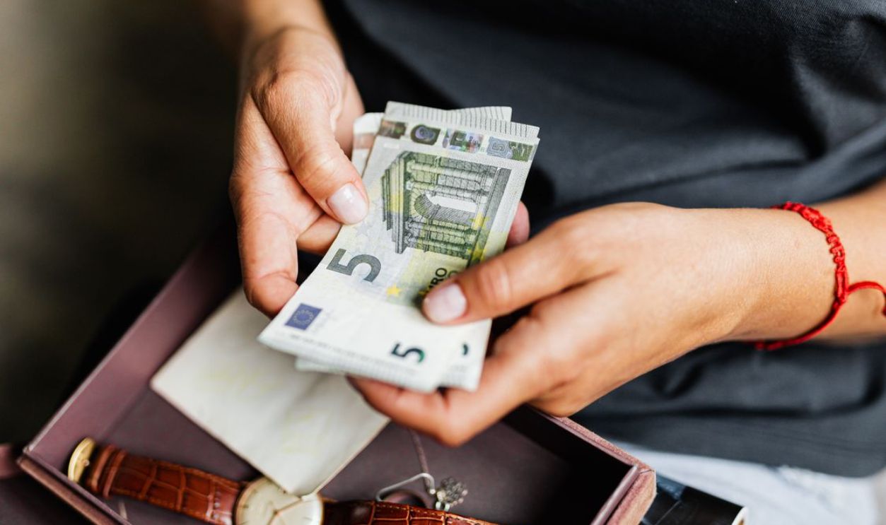 Close-up of hands counting euro notes above a wristwatch in a box.
