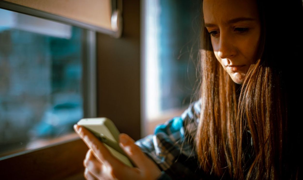 Young woman looking at smartphone with sunlight streaming in through a window.
