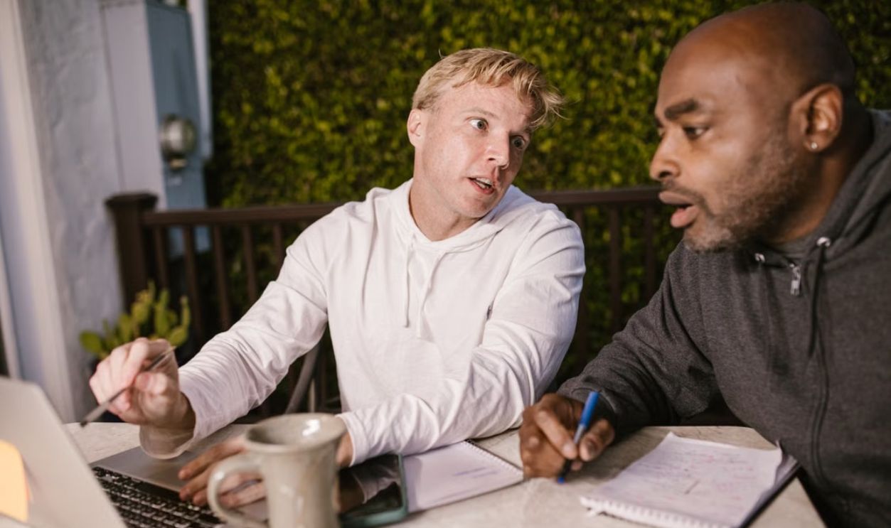 Two men collaborating on a project with a laptop outdoors, discussing ideas.