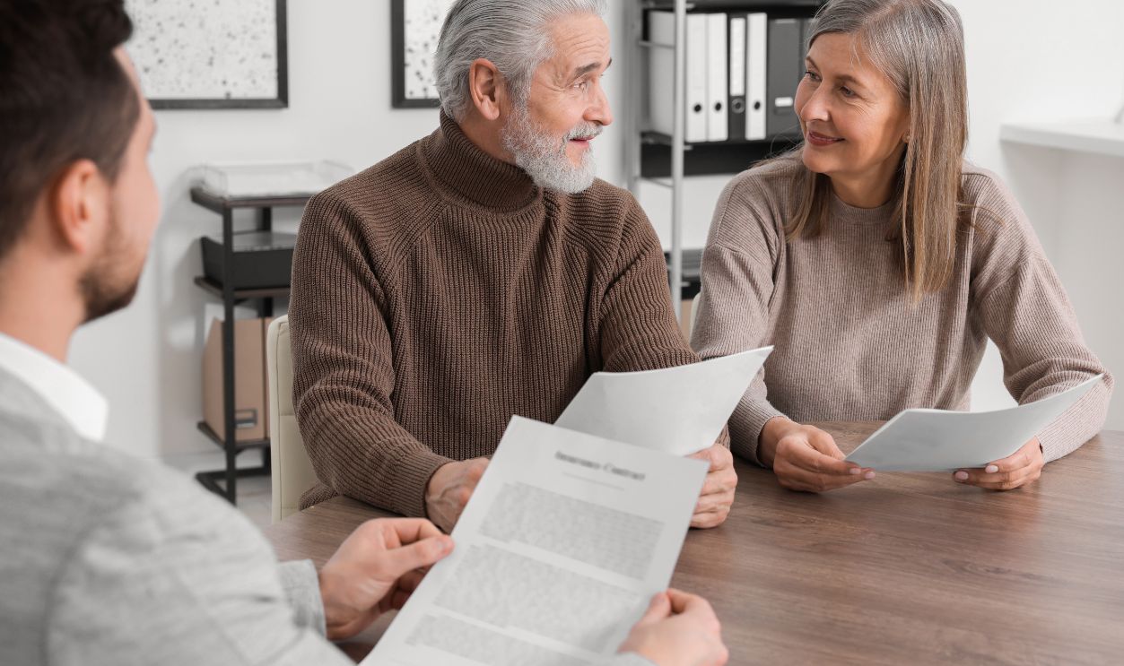 Elderly couple consulting insurance agent about pension plan at wooden table indoors