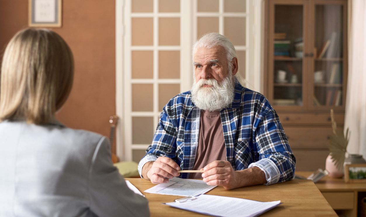 Shutterstock-2292594941, Serious senior man talking to financial advisor during their meeting at table with documents at home