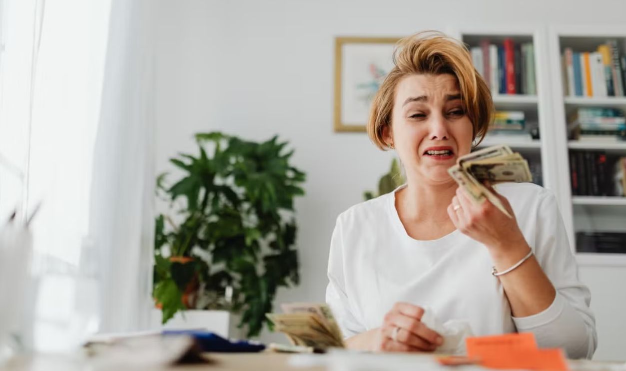 A woman looking stressed while counting money in a living room setting