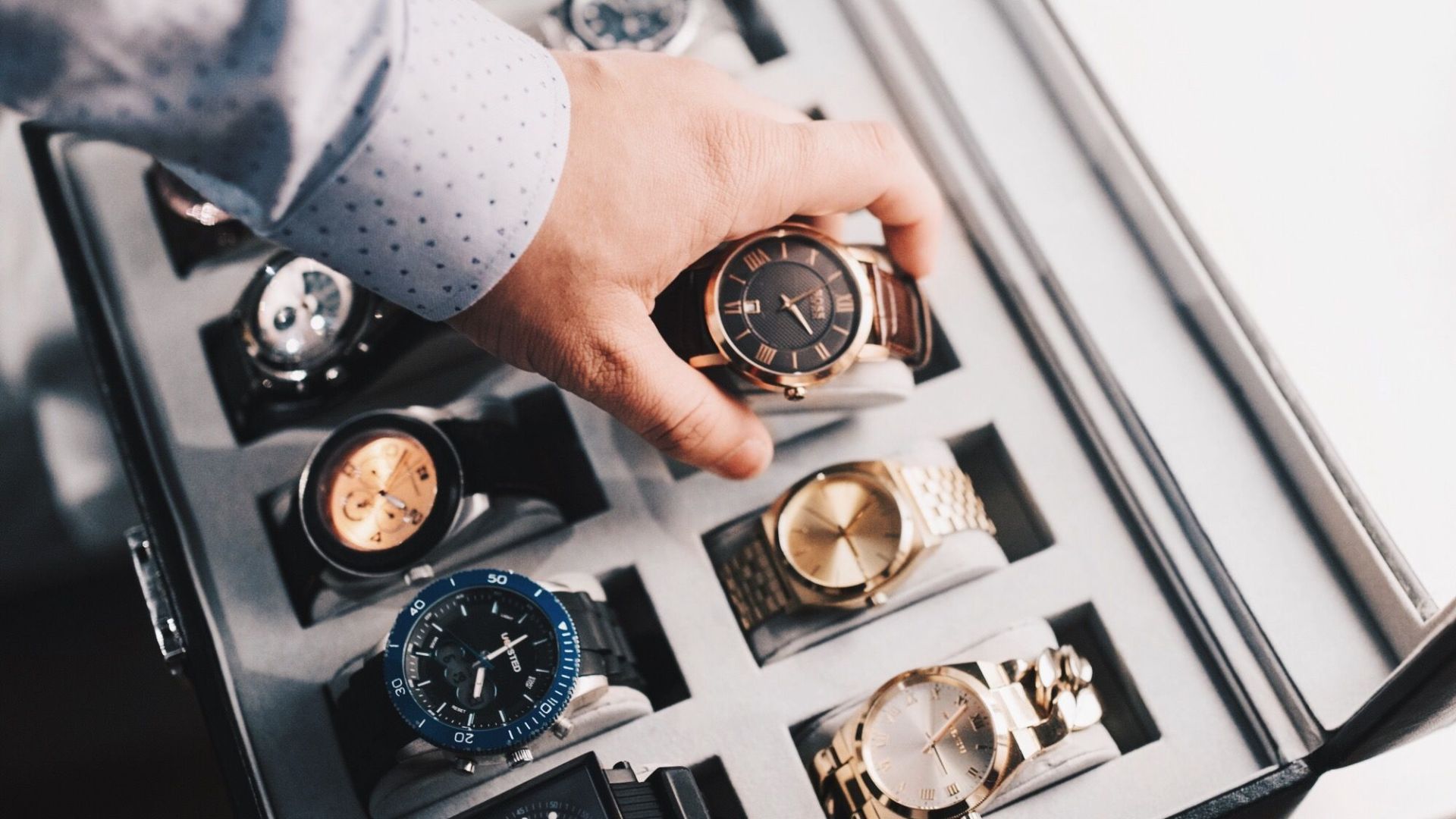 A sophisticated display of luxury watches in an elegant case with a hand selecting one.