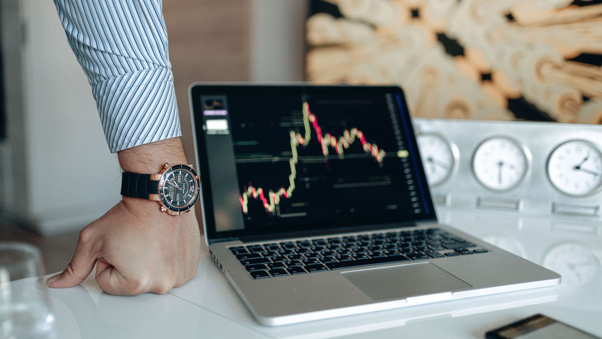 A sophisticated workspace featuring a laptop with a stock chart and a watch on a man's wrist.