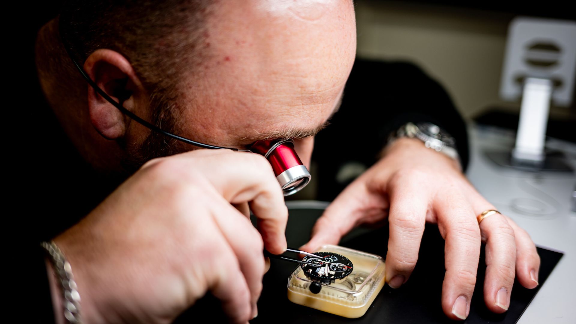 A professional watchmaker closely examines a watch mechanism with a magnifying glass.