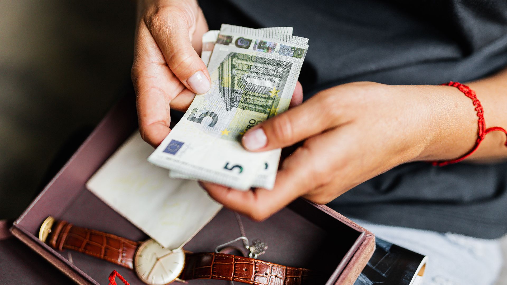 Close-up of hands counting euro notes above a wristwatch in a box.