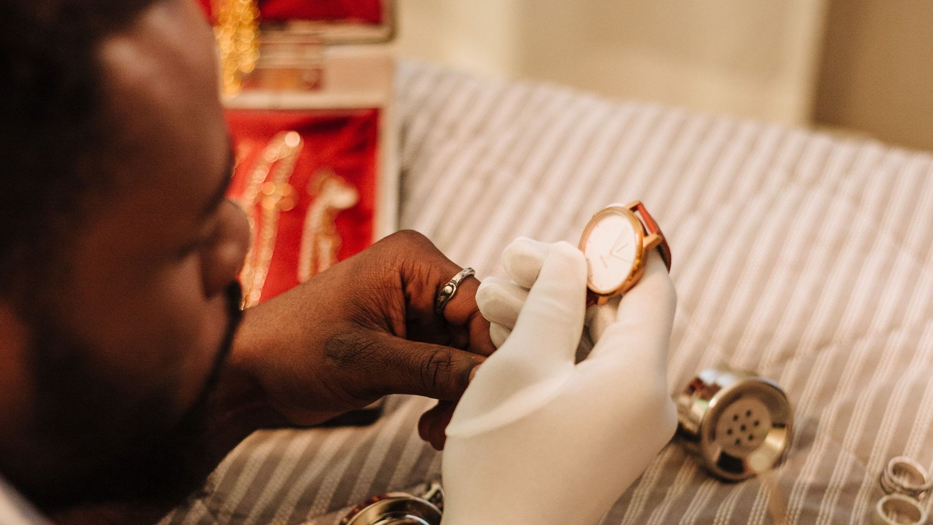 A man with gloves examines a vintage watch next to a retro telephone.
