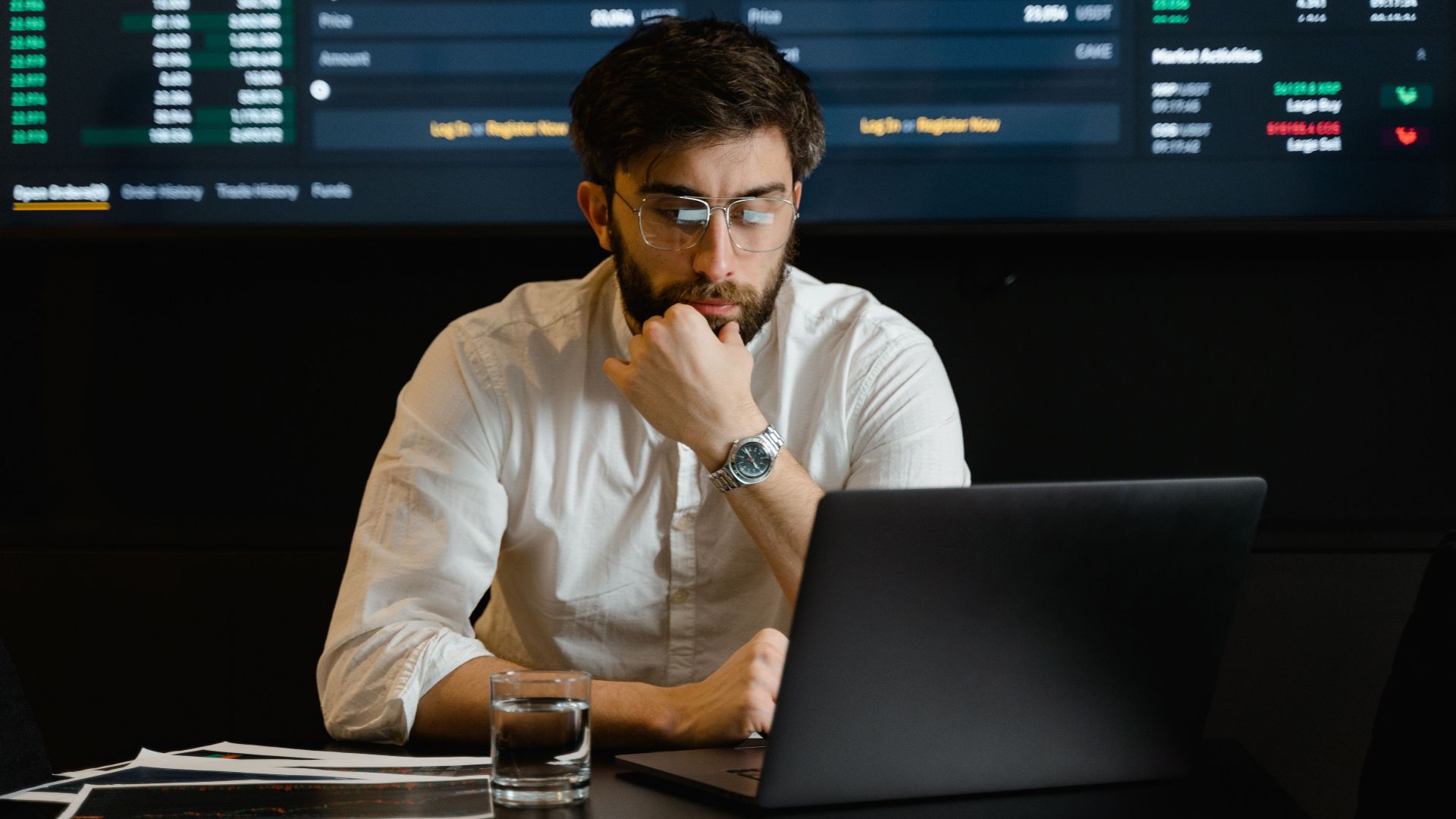A man intensely analyzing stock market data on a laptop in an office setting.