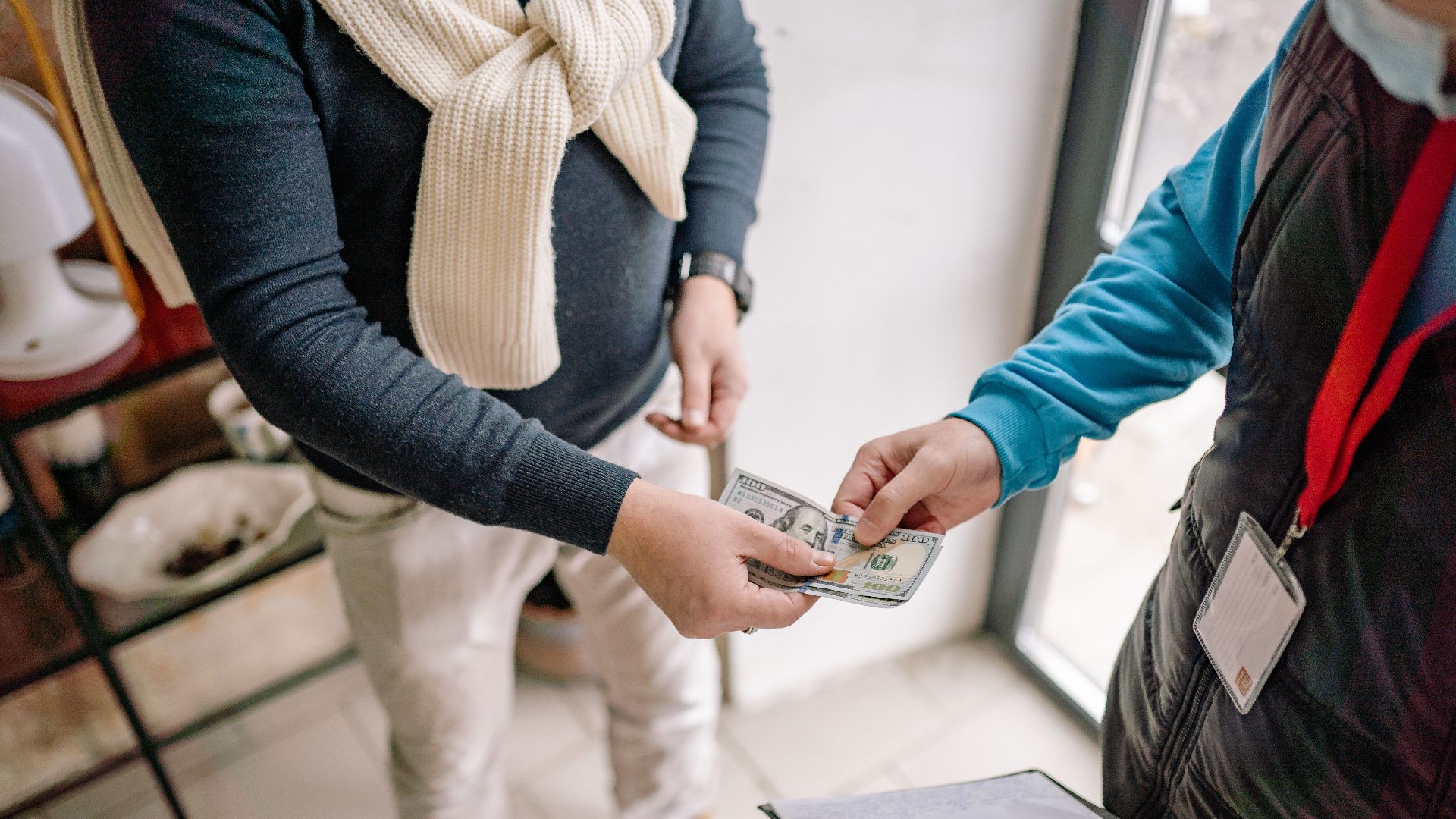 Close-up of hands exchanging cash during a transaction indoors, highlighting payment details.