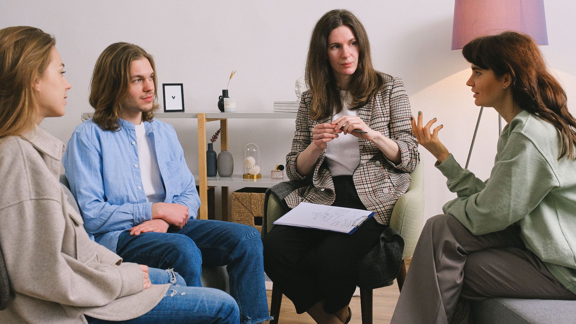 Female in casual clothes sitting on sofa and talking with psychologist and other people in group