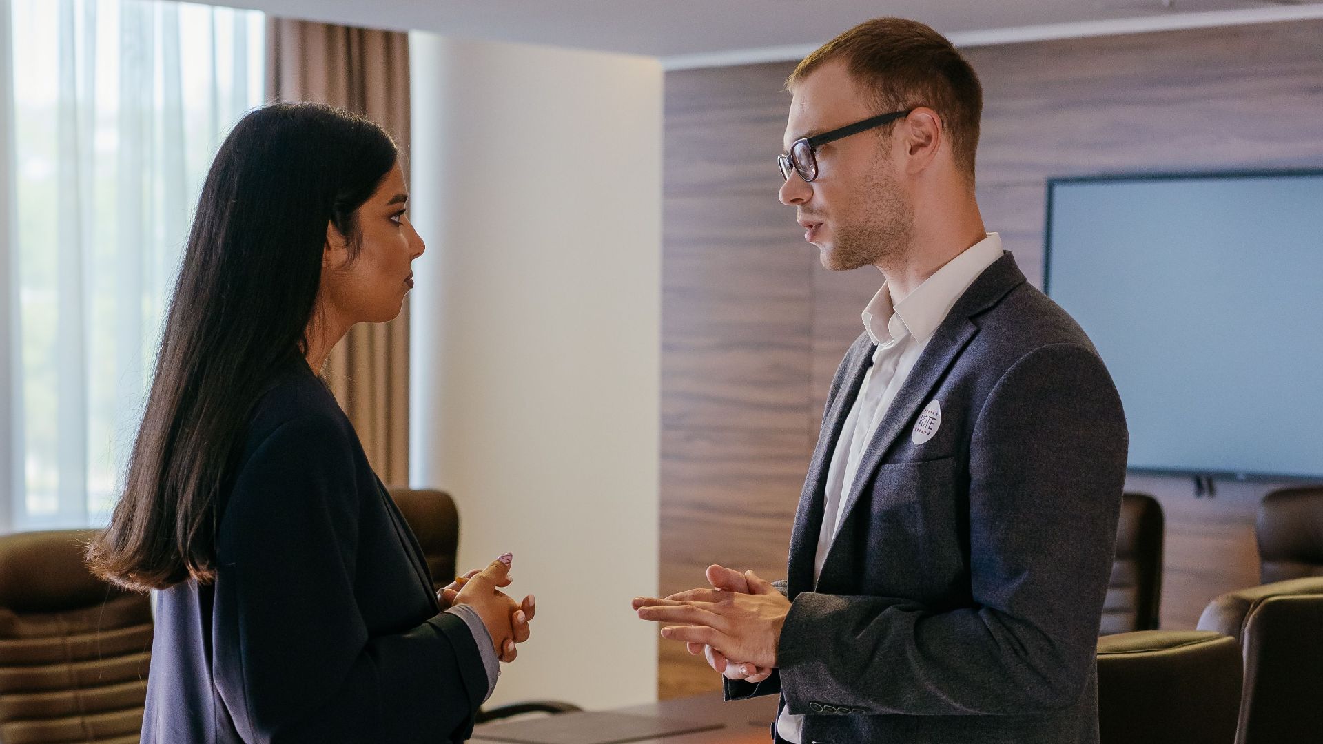 Two professionals engaged in discussion inside a modern conference room setting.
