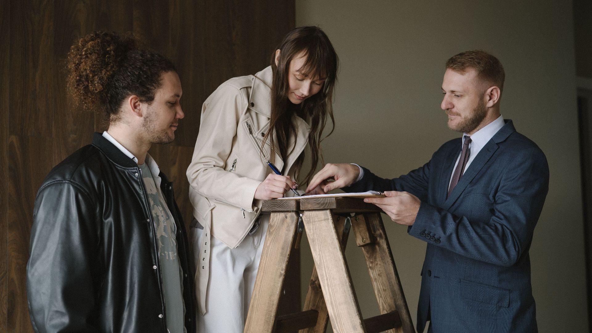 Three individuals signing a contract on a ladder inside a new house, symbolizing a real estate deal.