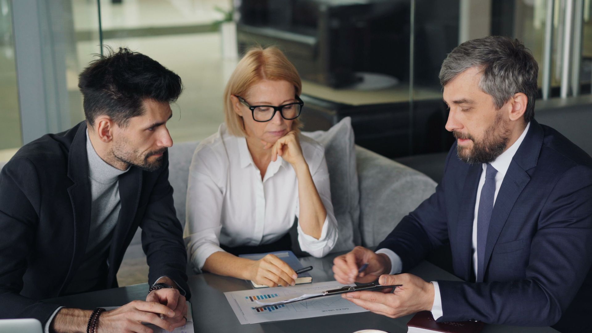 Three professionals engaged in a business discussion at an office table with coffee.