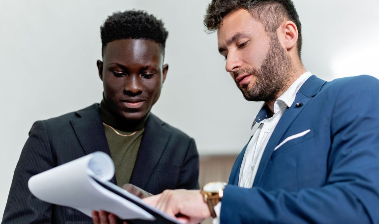 Two businessmen in suits discuss important documents in an office setting
