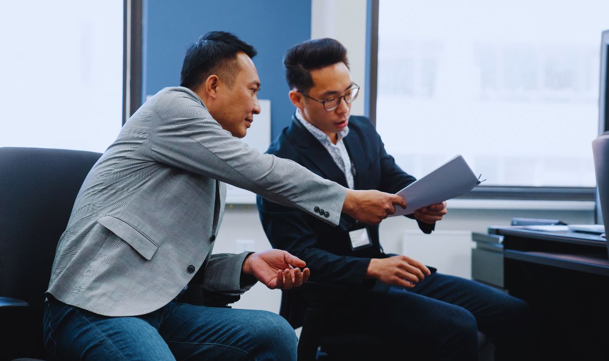 Two male colleagues exchanging documents in a modern office setting