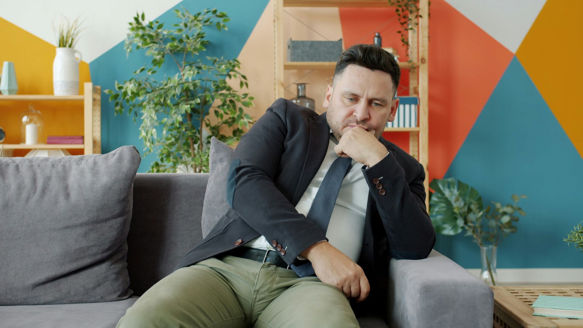 Man in suit sitting on couch looking thoughtful.
