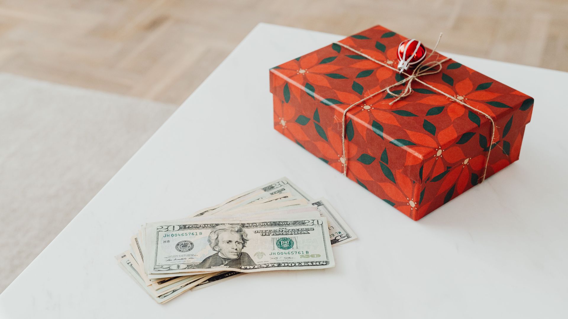A holiday-themed gift box with US dollar bills on a white table indoors.