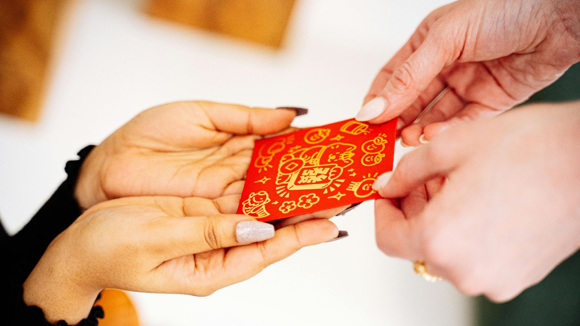 Hands exchanging a decorative red envelope for Lunar New Year, symbolizing good luck and prosperity.