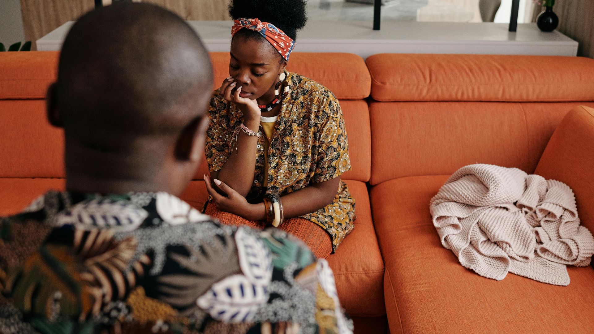 A thoughtful couple engaged in a deep discussion on a vibrant orange sofa in a modern living room.