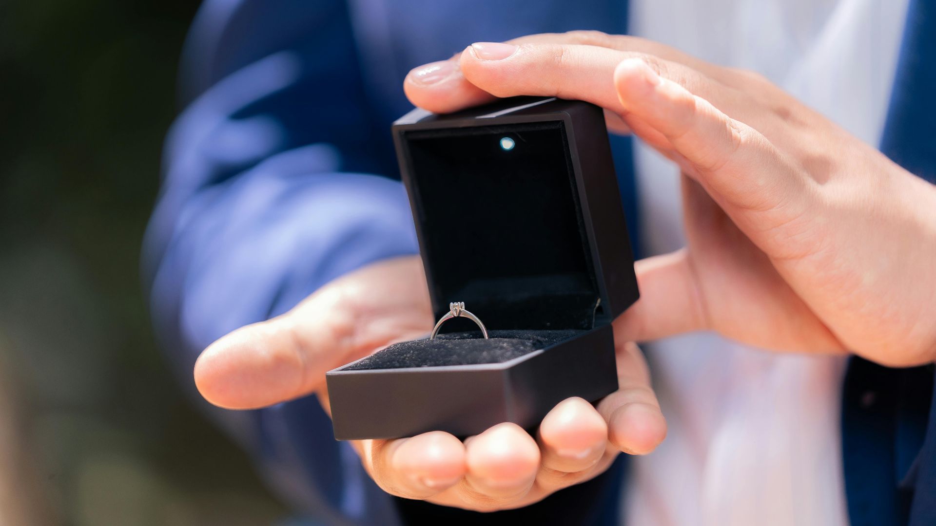 Close-up of a man holding a diamond engagement ring in a black box, symbolizing proposal.