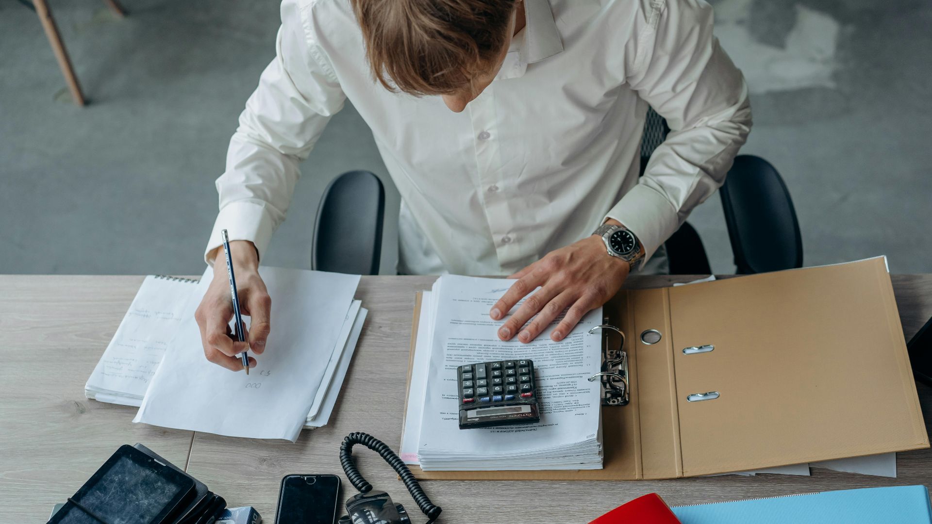 Man in an office reviewing financial papers with a calculator on a desk.