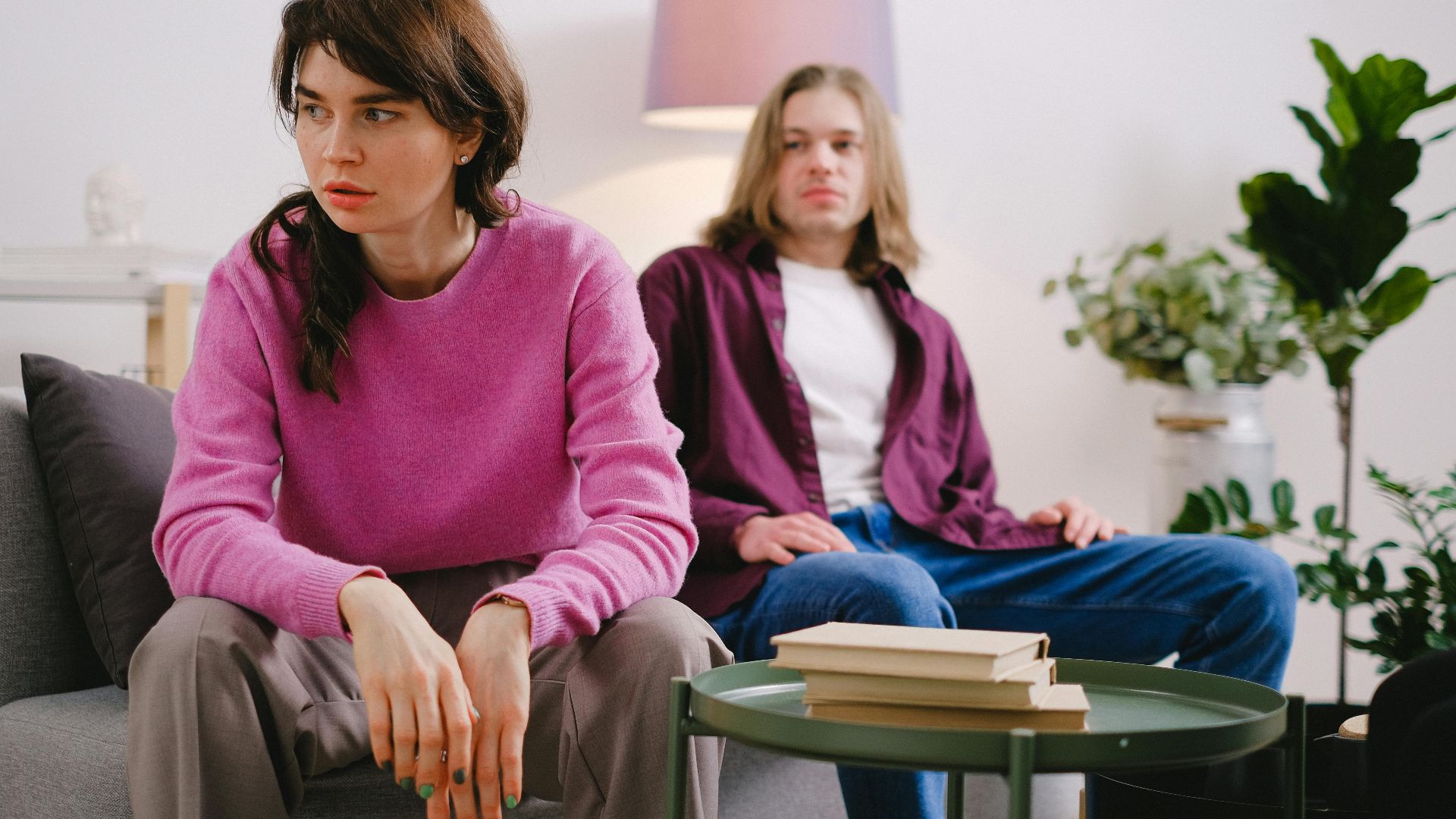 A couple sitting on a sofa with thoughtful expressions, surrounded by home decor.