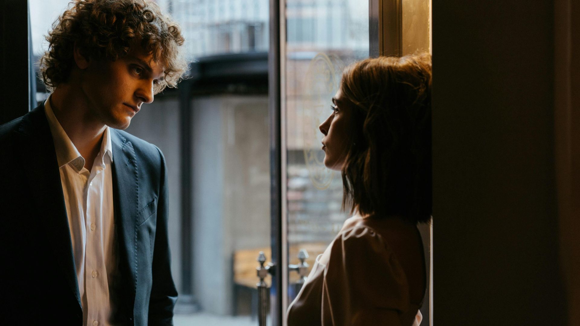 Man and woman dressed elegantly in conversation by a doorway, creating a romantic atmosphere.