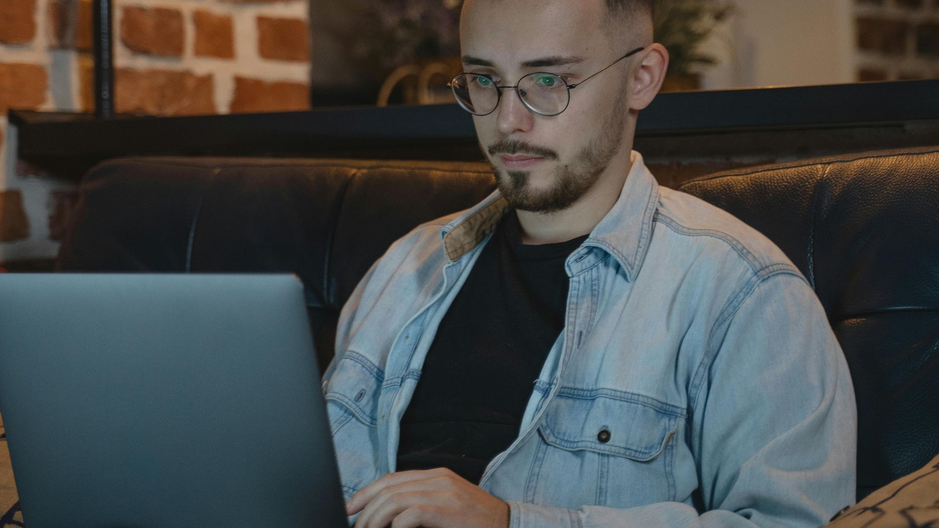 A man works on a laptop from a comfy couch in a stylish home setting.