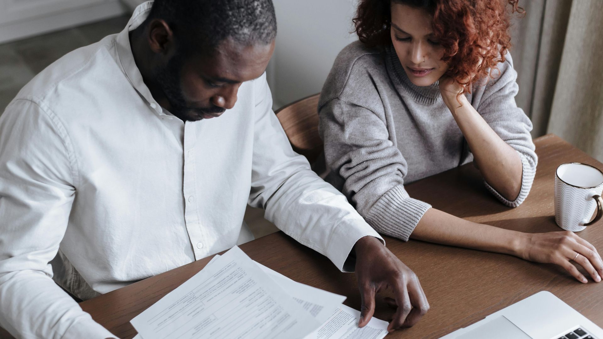 A couple reviews important documents together at a home desk with a laptop.