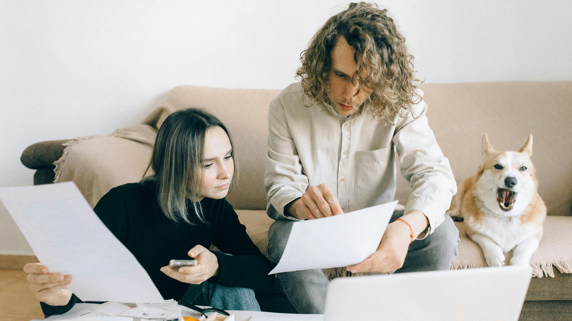 A couple working remotely at home with documents and a dog on the sofa.