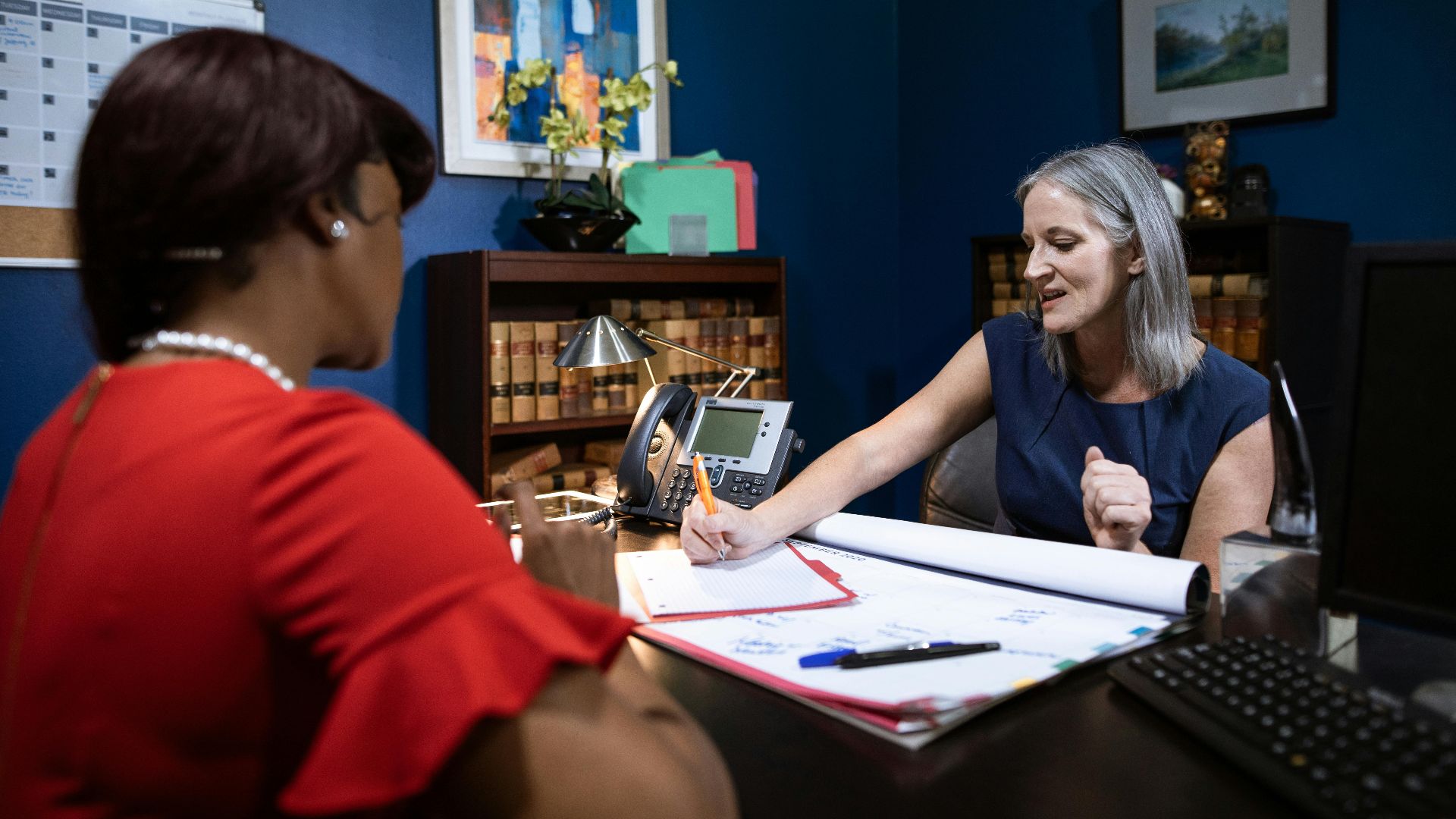 Two women engage in a work discussion in a modern office setting, captured candidly.