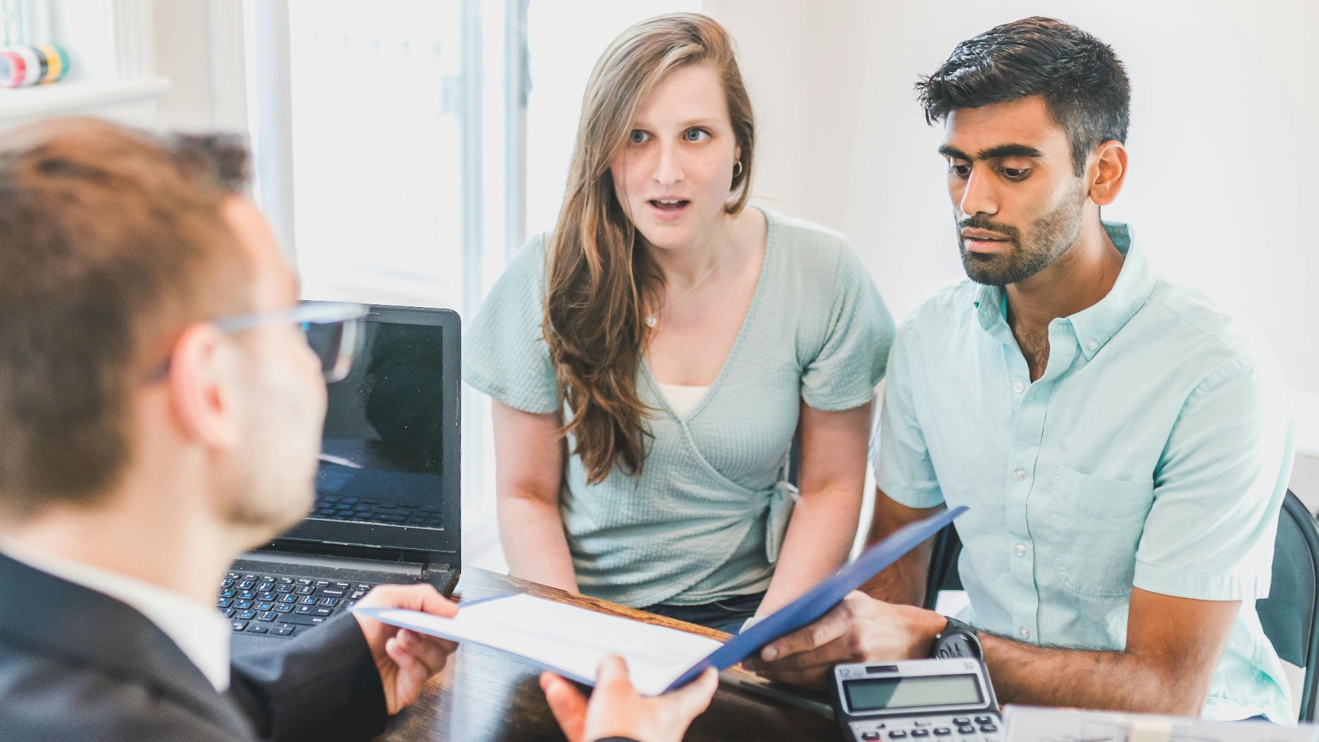 A young couple discusses home buying options with a real estate agent indoors.