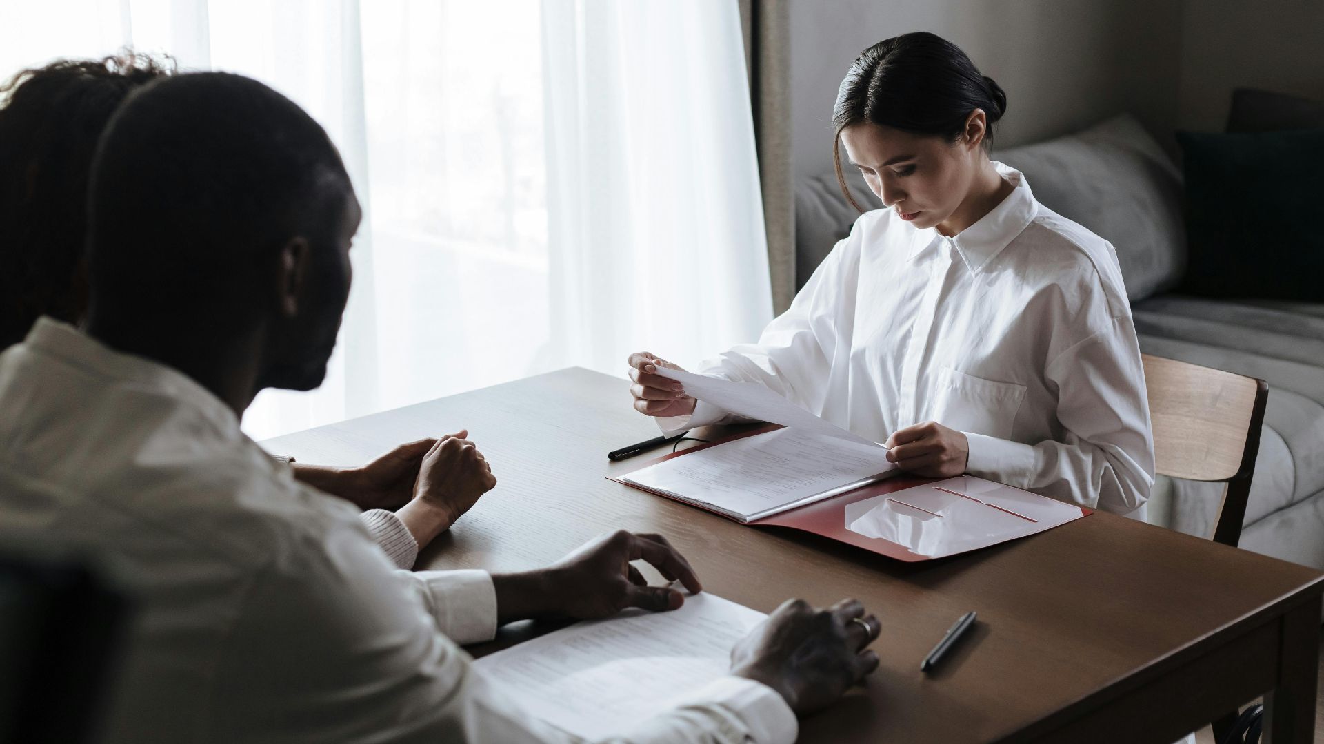 A professional woman reviews documents with a couple at home, indicating a collaborative decision-making process.