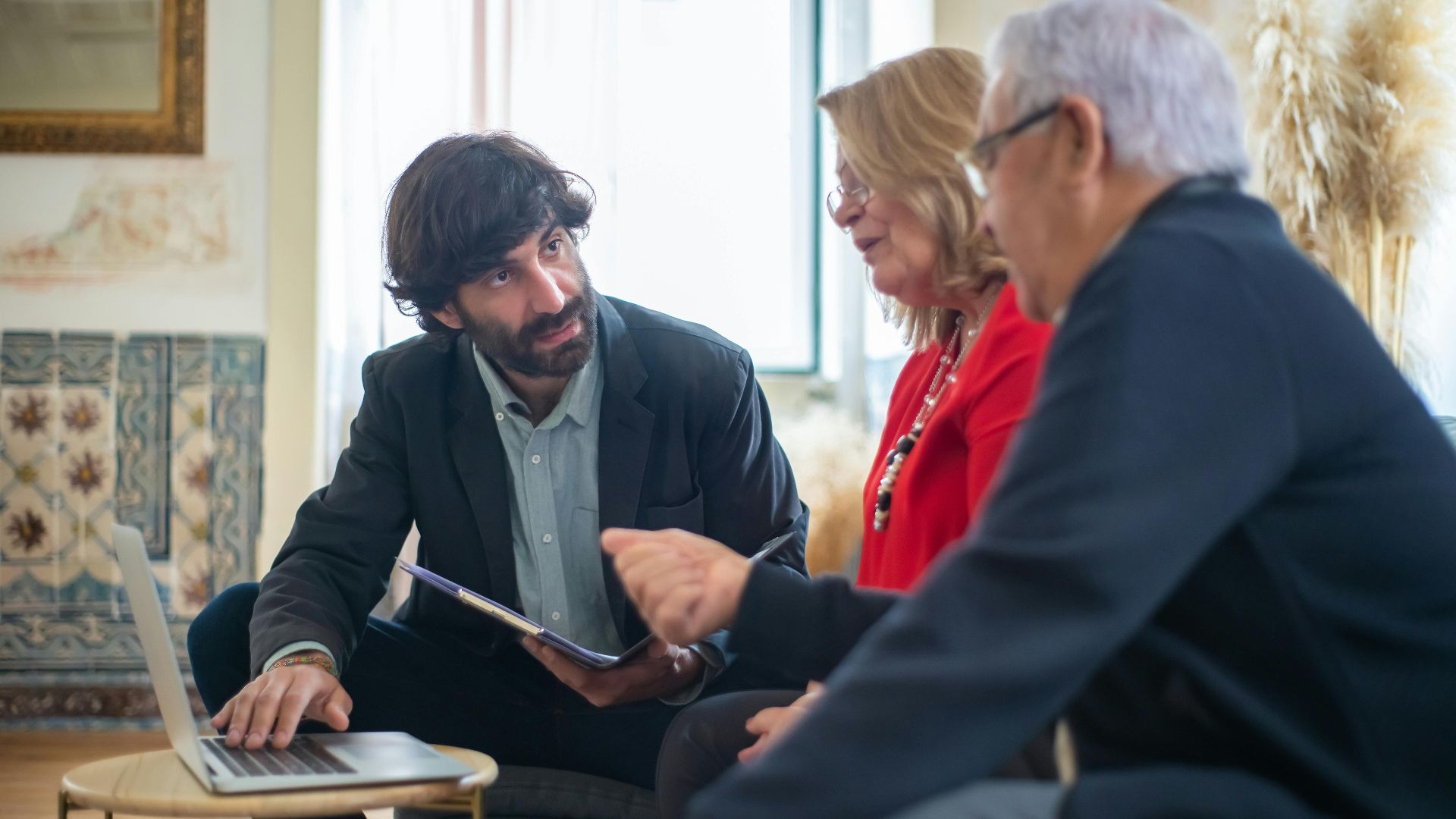 Three adults having a business meeting indoors, discussing ideas around a laptop.
