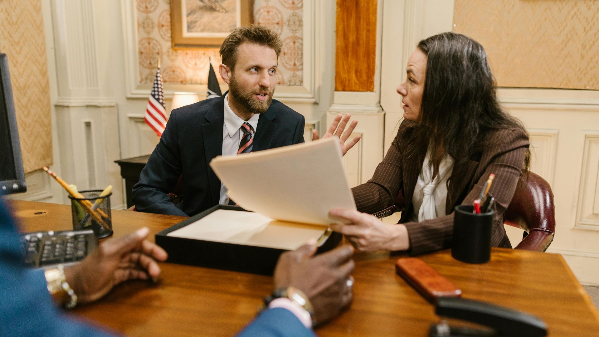 Diverse group in a corporate office engaged in a formal meeting. Professional attire and documents suggest a business discussion.