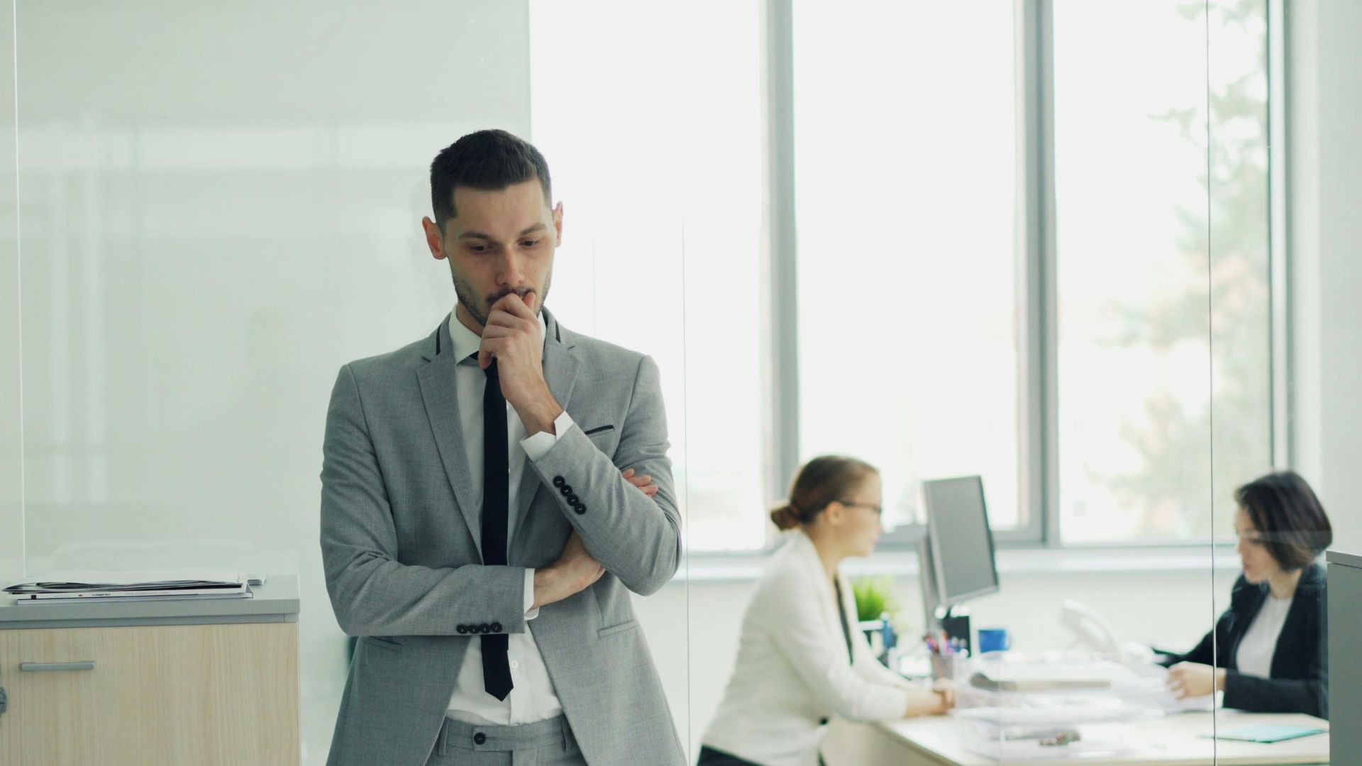 Thoughtful businessman in a modern office setting with colleagues working in the background.