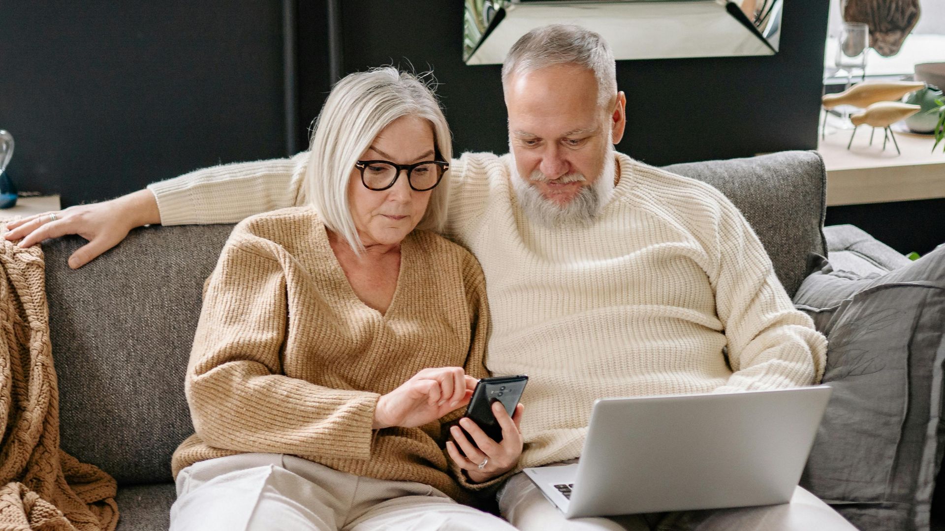 Elderly couple enjoying digital gadgets on the sofa in a cozy home setting.
