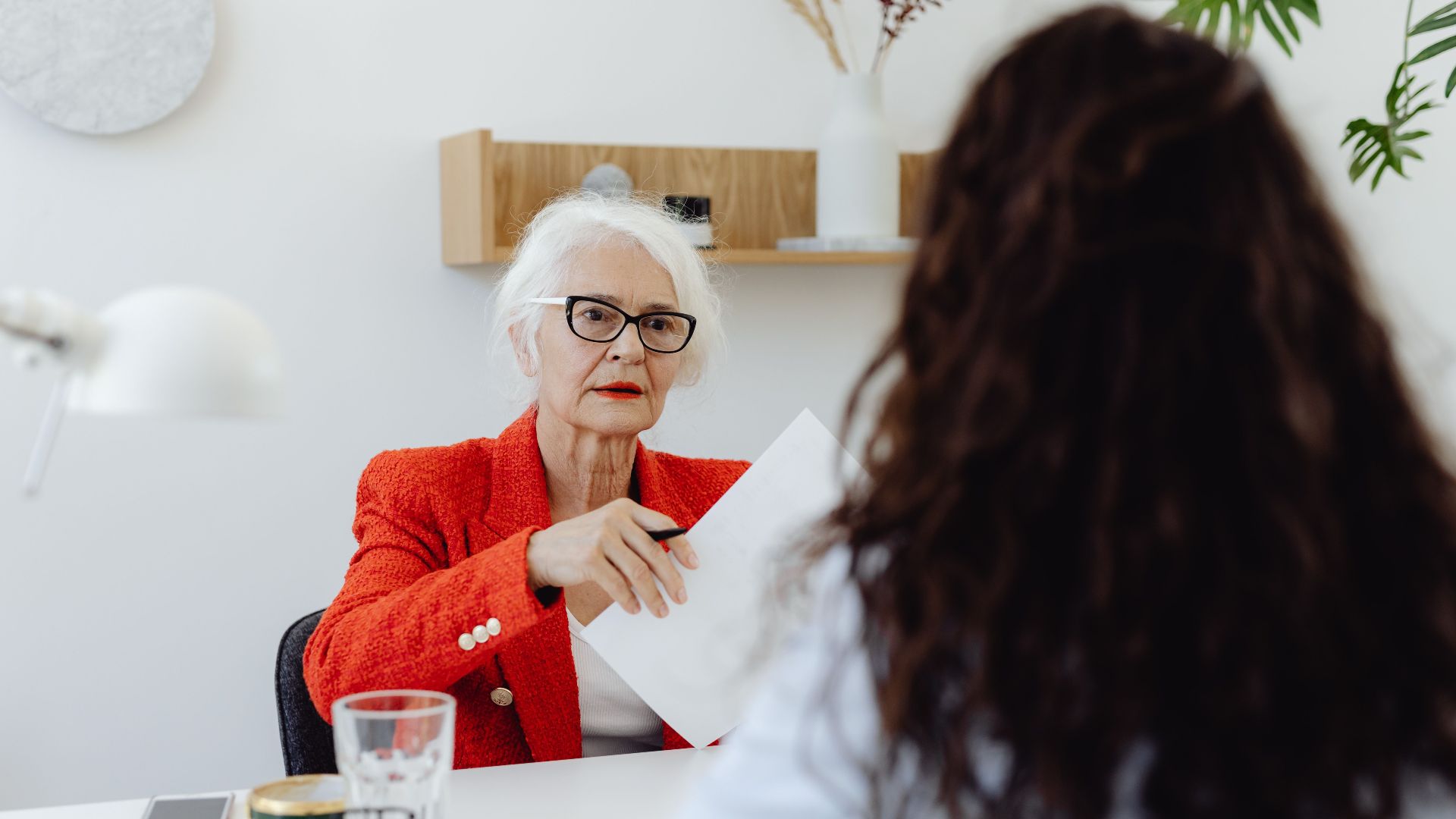 Senior businesswoman in red blazer engaging in a document review meeting in a modern office setting.