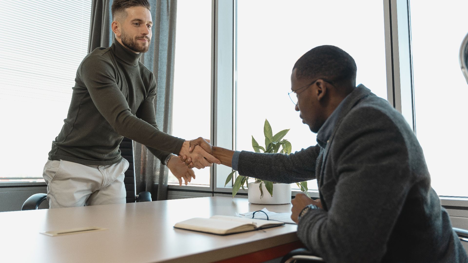 Two businessmen shaking hands in a modern office after a successful meeting or interview.