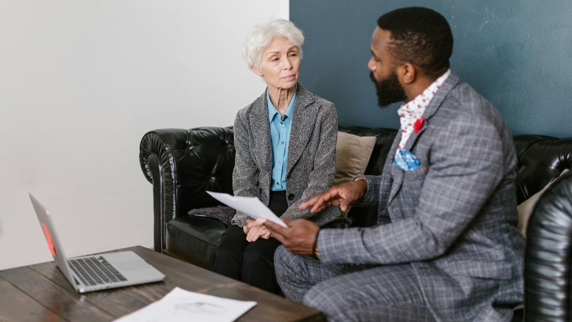 An elderly woman and a man in a professional meeting discussing documents indoors.