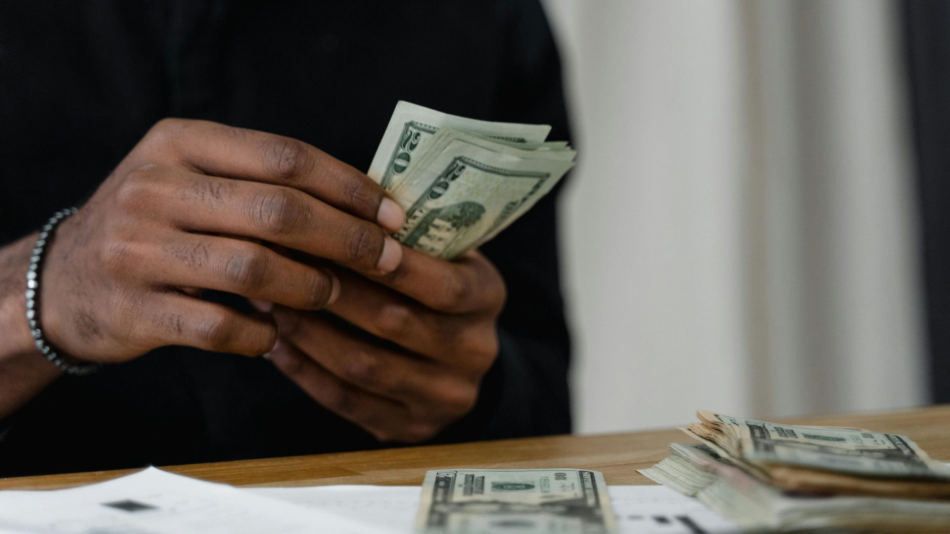 Adult counting dollar bills at a desk, focused on money management and finance.