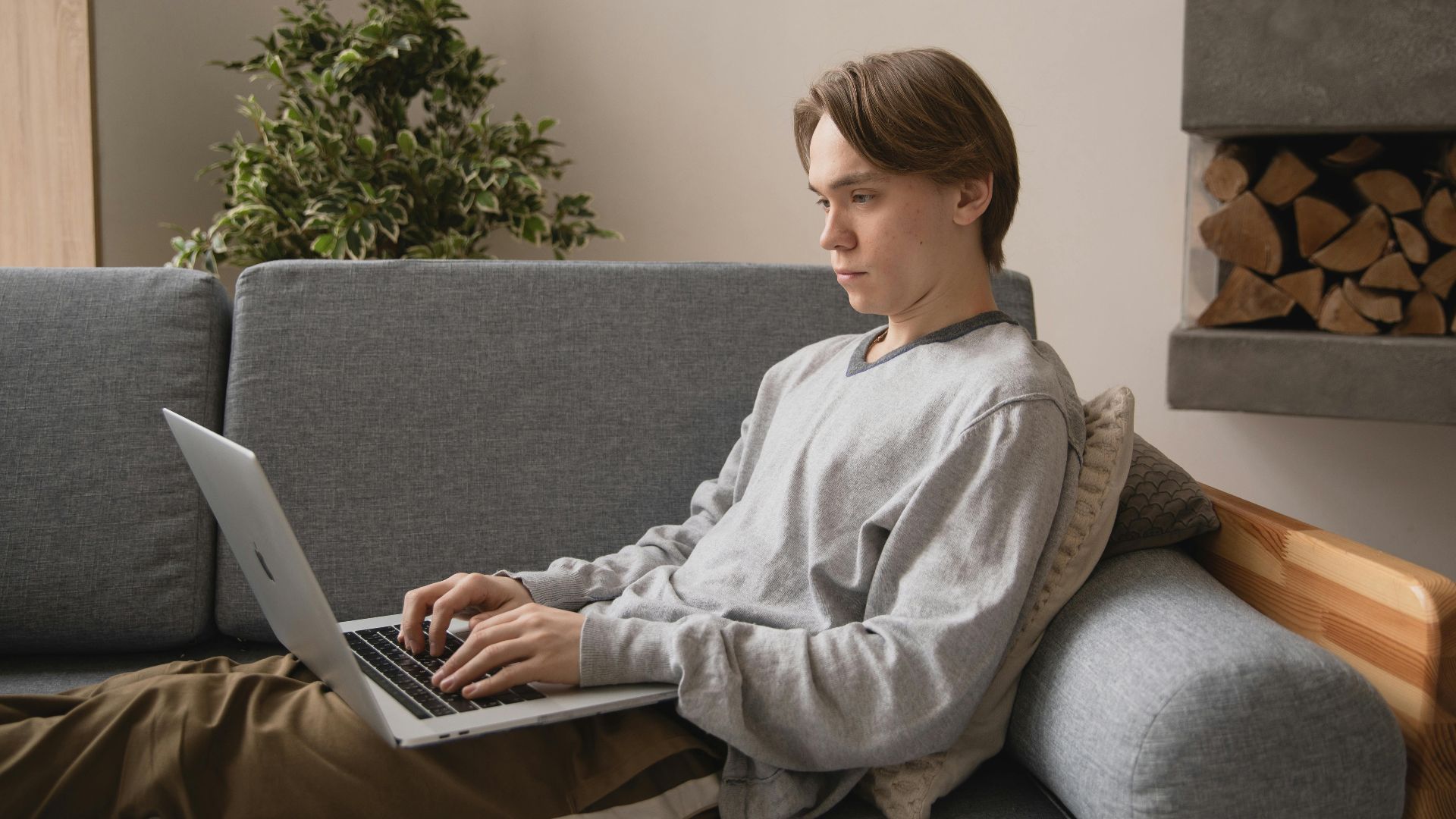 A young man sits comfortably on a sofa typing on a laptop, embodying remote work lifestyle.