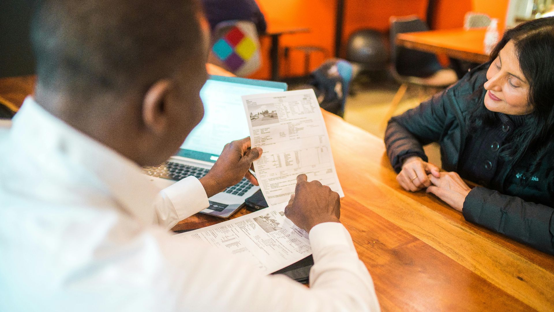 Two adults discussing documents in a business setting indoors.