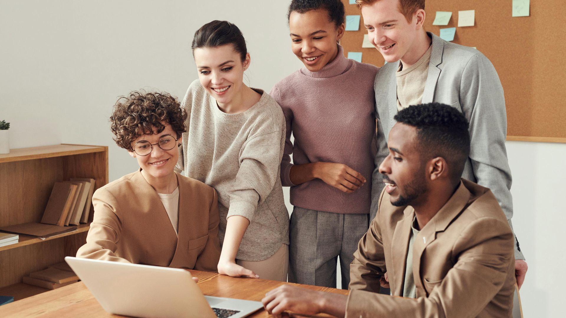 Group of diverse professionals engaged in brainstorming session around a laptop indoors.