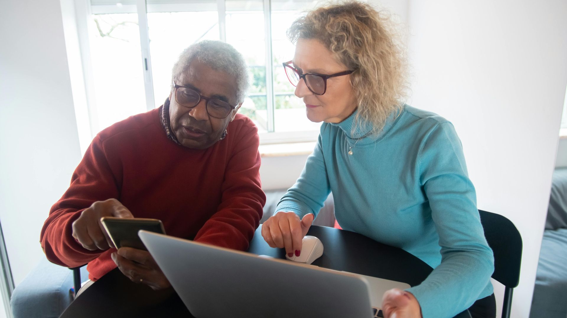 Elderly man and woman sitting together, engaging with technology indoors.