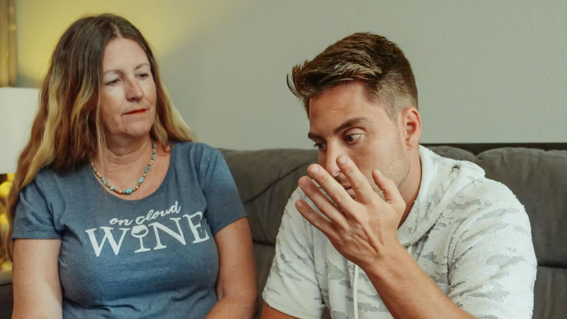 A mother and son engage in a deep conversation on the living room couch, conveying strong emotions.