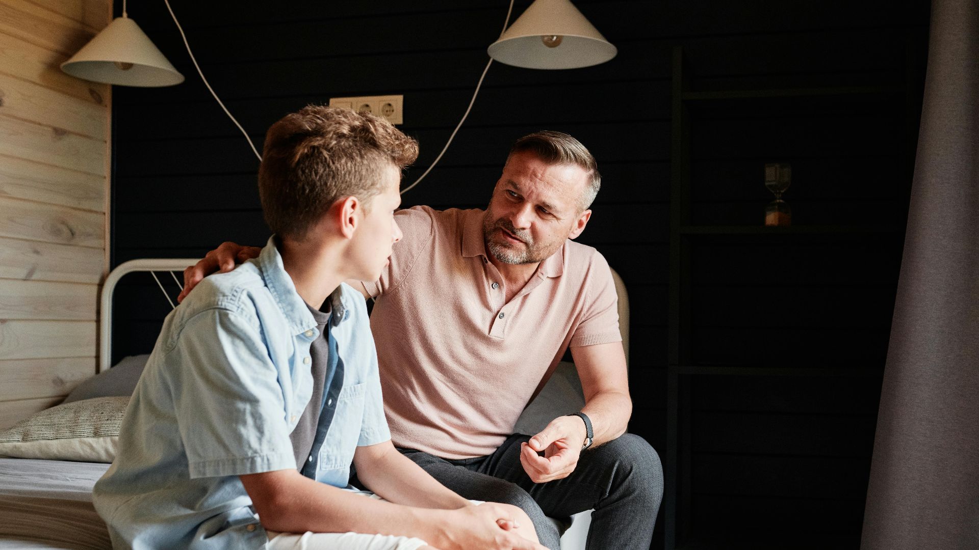 A father bonding with his teenage son in a cozy bedroom, sharing advice and conversation.